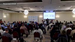 Wide Shot of crowd sitting in a large conference room. Projection screen with Walk as One Logo. 